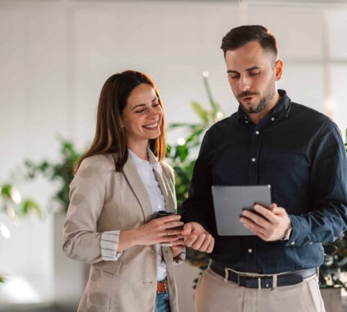 Businesspeople with tablet discussing report at green modern office. Portrait of professional confident businesspeople standing at enterprise office with tablet in hands and discussing report. Successful colleagues collaborating on a project and working as a team.